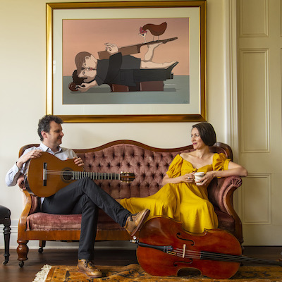 Slava and Sharon Grigoryan relaxing on a couch under an abstract painting depicting two lovers with a guitar and cello
