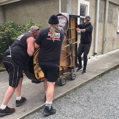 A grand piano being pushed up a path by three men